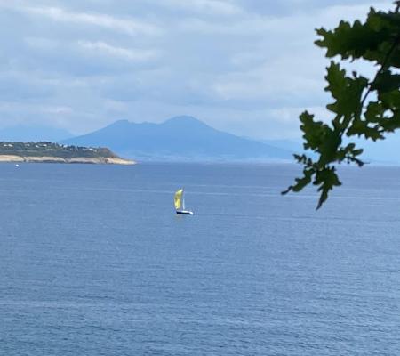 Lone sailboat on the sea, Mount Vesuvius in distance, serene and contemplative atmosphere.