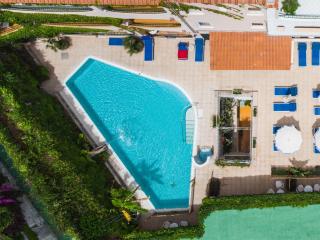 Vista dall'alto di una piscina con lettini e ombrelloni, atmosfera di relax estivo.