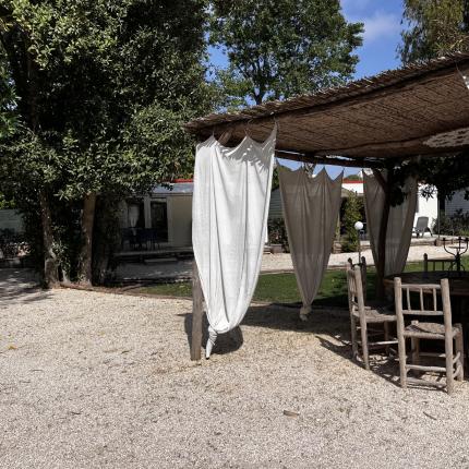 Gazebo rustico con tende bianche, sedie in legno e atmosfera serena.
