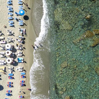 Crowded beach, colorful umbrellas, crystal-clear sea, gentle waves.