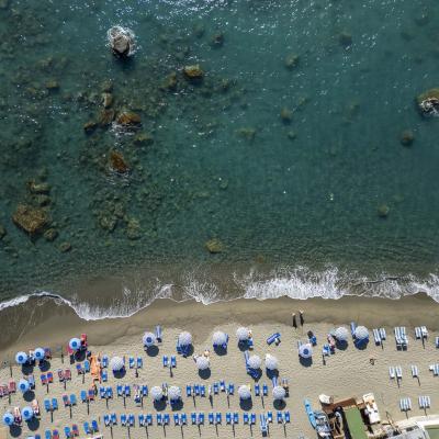 Crowded beach, colorful umbrellas, crystal-clear sea, gentle waves, lively summer atmosphere.