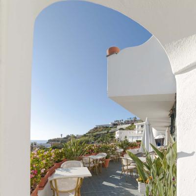 Sunny terrace with sea view, colorful flowers, and inviting tables.