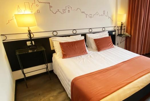 Gemütliches Zimmer mit Doppelbett, warmen Lampen und bunten Vorhängen.