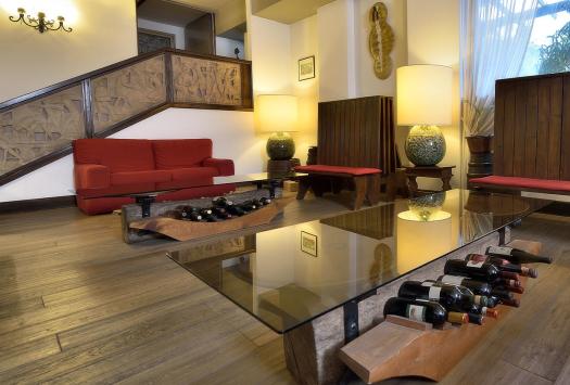Gemütliches Wohnzimmer mit roten Sofas, Glastisch und Weinflaschen.