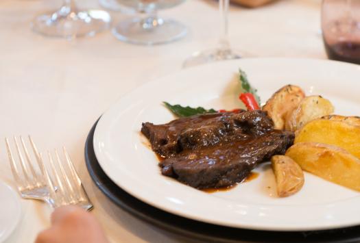 Eleganter Teller mit Fleisch in Sauce und Bratkartoffeln, edle Essensatmosphäre.