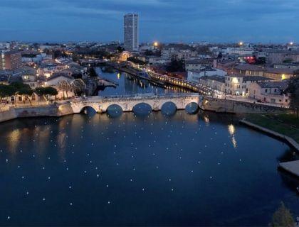 Ponte antico su fiume illuminato, città vibrante al crepuscolo.