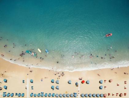 Spiaggia affollata con ombrelloni colorati, mare blu e atmosfera estiva vivace.