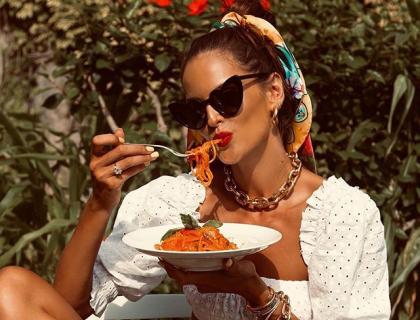 Donna elegante mangia spaghetti al sole, indossa occhiali e foulard colorato.