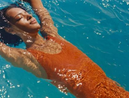 Donna rilassata galleggia in piscina, sole splendente, acqua cristallina.