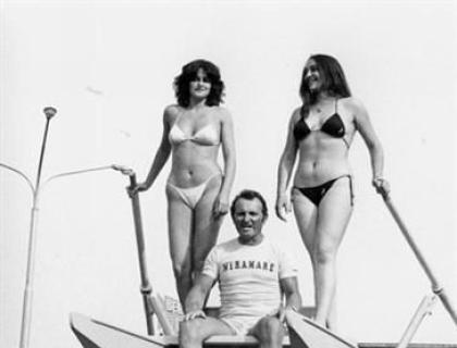 Due donne in bikini e un uomo su un furgone Fiat, atmosfera estiva e festosa.
