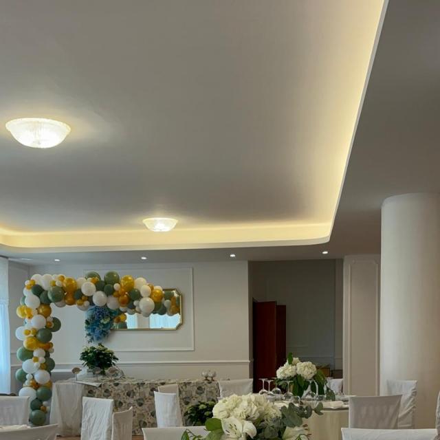 Sala elegante con tavoli decorati e arco di palloncini colorati.