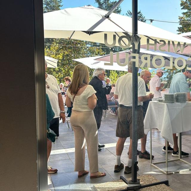 Persone in fila per buffet all'aperto, atmosfera conviviale e soleggiata.