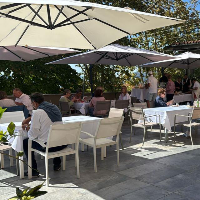 Terrazza soleggiata, conversazioni vivaci sotto ombrelloni bianchi, atmosfera rilassata e conviviale.