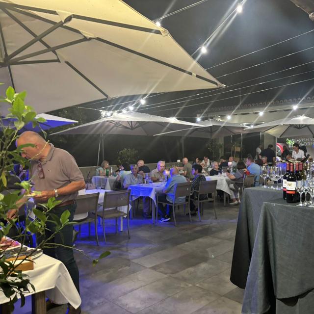 Cena all'aperto, atmosfera festosa con luci soffuse e tavoli elegantemente apparecchiati.