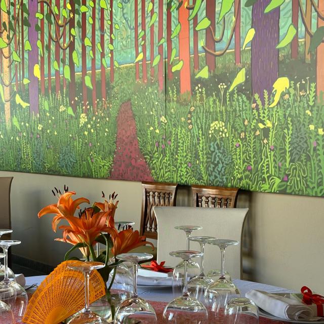 Tavola elegante con fiori arancioni, calici e sfondo boschivo colorato.