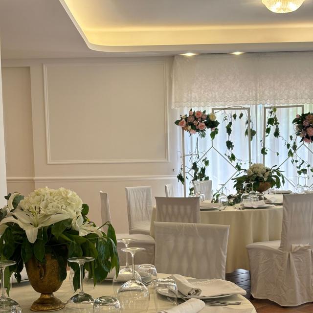 Elegante sala da pranzo con tavoli decorati e fiori bianchi e rosa.