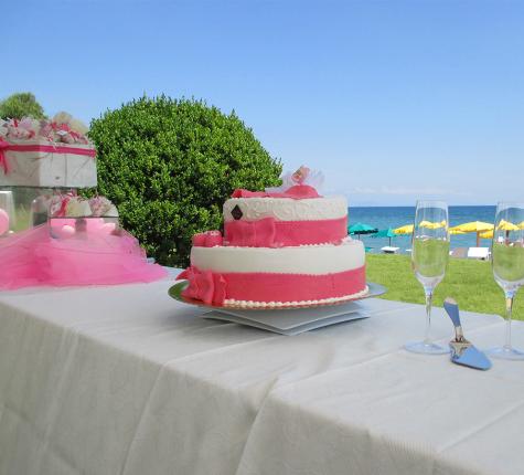 Pink and white cake on outdoor table, sea view.
