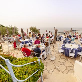 Outdoor dinner with sea view, people seated at tables.