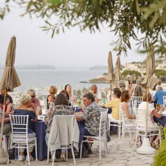 Outdoor dinner with sea view, people seated at tables.