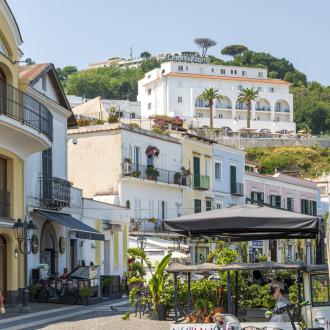 Picturesque street with colorful buildings and shops, view of a hilltop hotel.