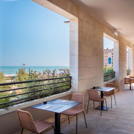 Terrazza con vista mare, tavoli e sedie per mangiare all'aperto.