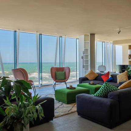 Modern living room with sea view, furnished with plants and colorful furniture.