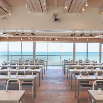 Modern conference room with sea view, arranged tables and chairs.