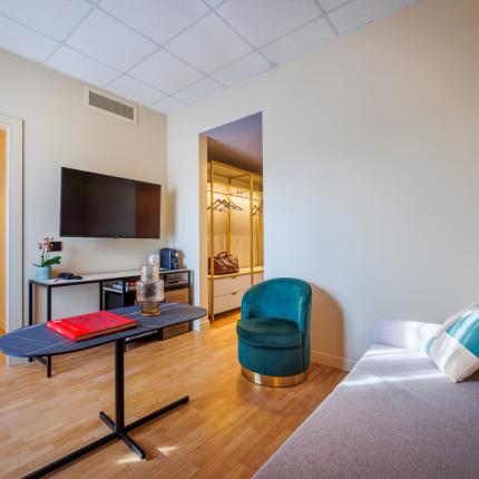 Elegant living room with TV, green chair, and access to the bedroom.