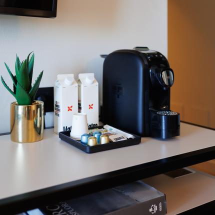 Coffee corner with machine, capsules, cups, and plants.