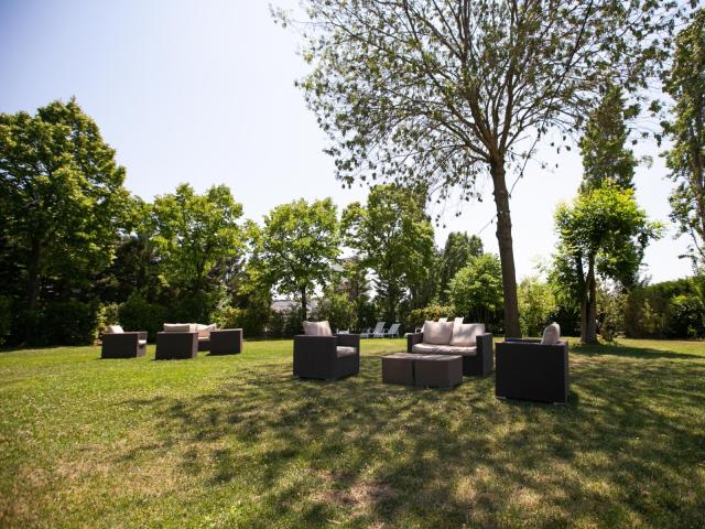 Giardino con mobili da esterno sotto un albero, cielo sereno.