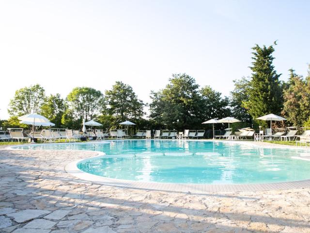 Piscina all'aperto con lettini e ombrelloni, circondata da alberi.