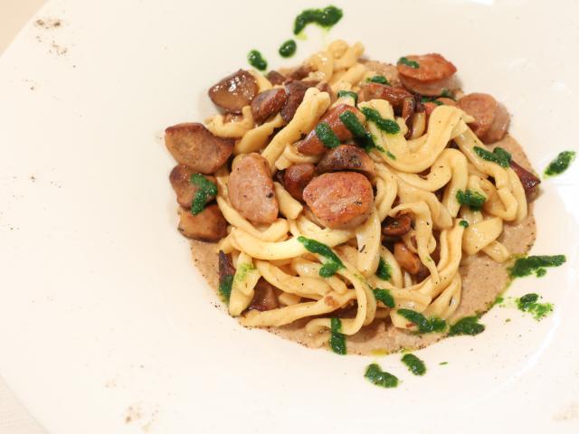 Pasta con salsiccia e funghi, guarnita con salsa verde.