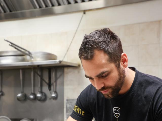 Cuoco prepara un piatto in cucina professionale.