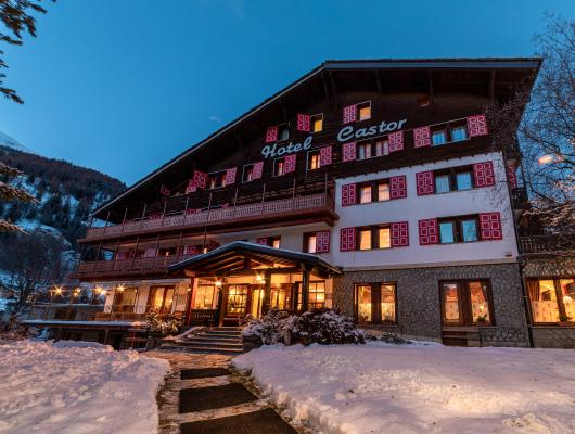 Hotel di montagna con neve, luci calde e atmosfera accogliente.