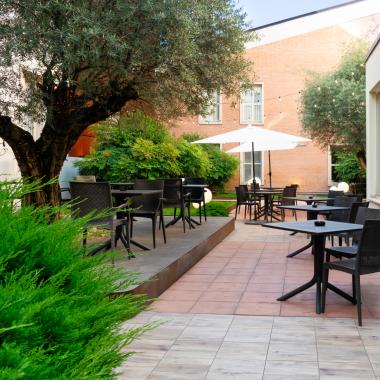 Terrazza esterna con tavoli, sedie e ombrelloni bianchi.