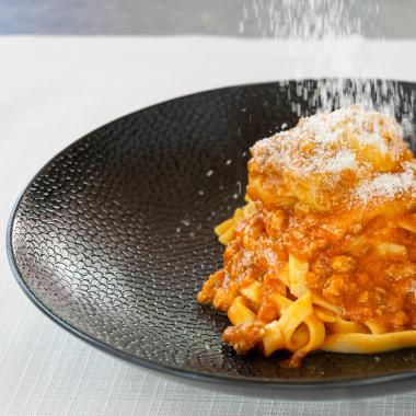 Tagliatelle al ragù con parmigiano su piatto nero.