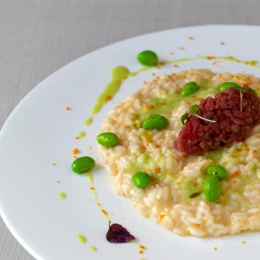 Risotto cremoso con tartare e fave, guarnito con erbe fresche.