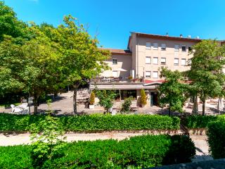 Giardino con sedie e alberi, edificio beige sullo sfondo.