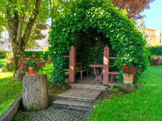 Giardino con gazebo di edera e fiori rossi su tronchi.