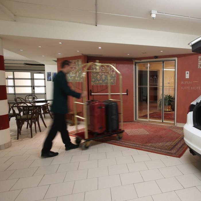 Luxury hotel, luggage on cart, white car open, elegant atmosphere.