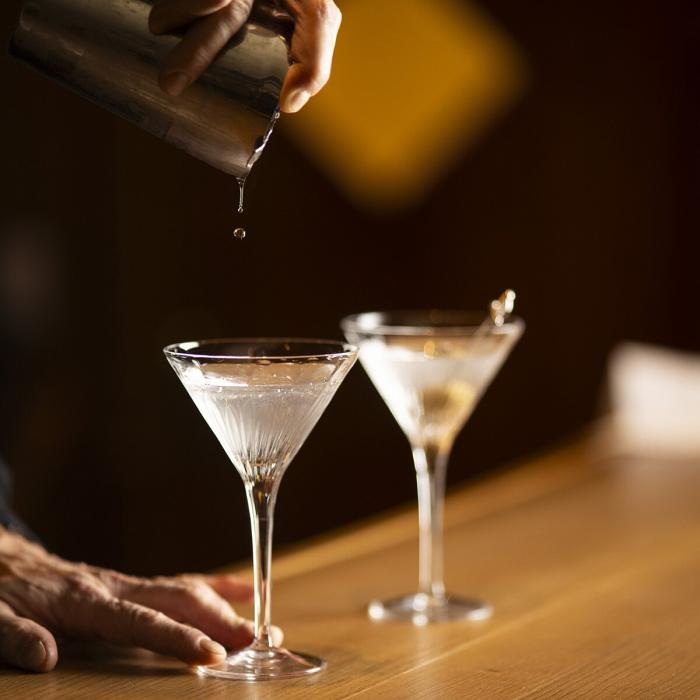 Hand pours elegant cocktail into glass on wooden bar.