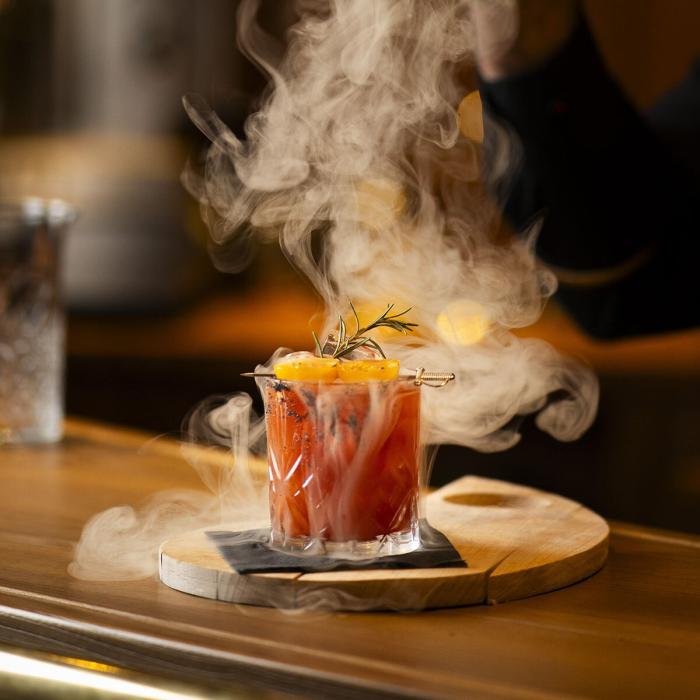 Steaming cocktail with rosemary and citrus on a wooden table.
