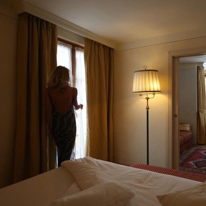 Woman in elegant dress gazes at morning light from a cozy hotel window.