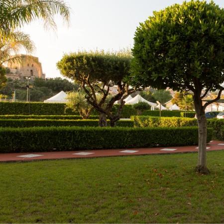 Giardino con alberi, siepi e edificio sullo sfondo.