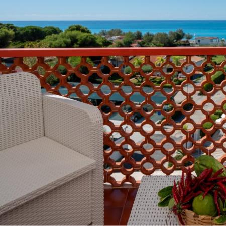 Balcone con vista mare, sedie bianche e cesto di frutta.