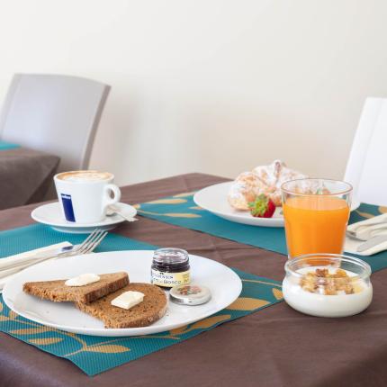 Frühstück mit Brot, Butter, Marmelade, Saft und Cappuccino.