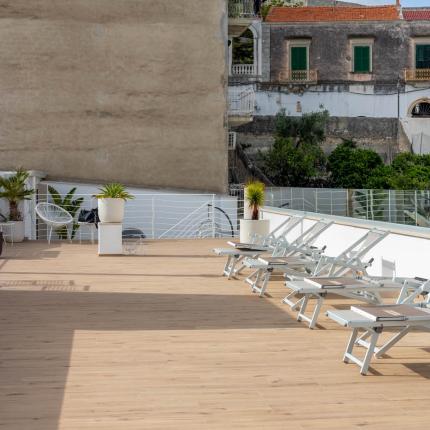 Terrasse mit Liegestühlen und Pflanzen, Blick auf historische Gebäude.