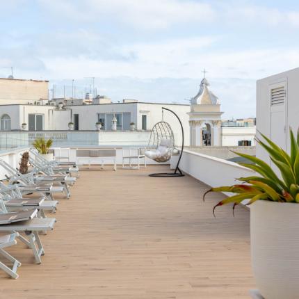 Terrasse mit Liegestühlen und Schaukelstuhl, Blick auf historische Gebäude.