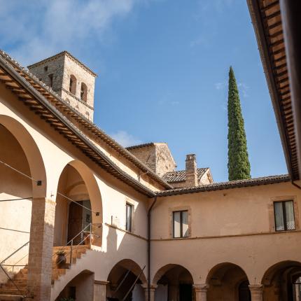 Cortile antico con colonne e torre in pietra, cipresso sullo sfondo.
