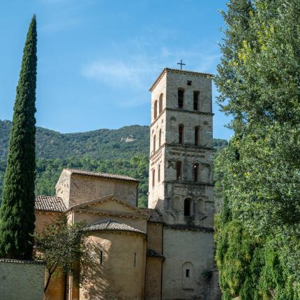 Antica chiesa con campanile, circondata da verde e montagne.